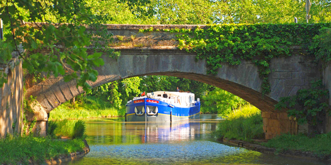 French Hotel Barge Enchante on the canal du midi Summer plans - French Hotel Barge Enchante approaching pretty bridge on the canal du midi in the south of France